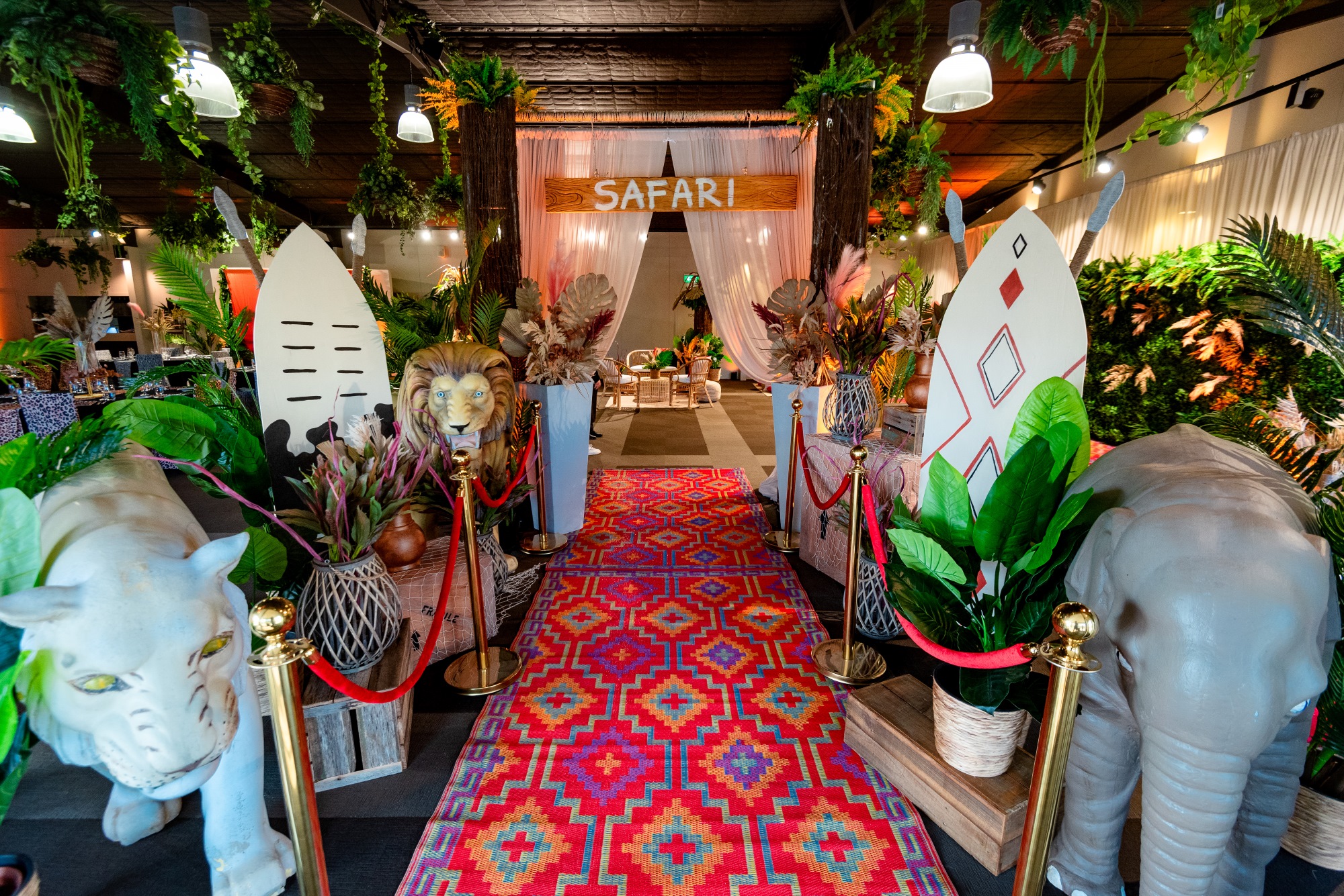 Inside the Leopard Lodge with a menagerie of tribal African and animal props in the foreground, a red carpet and white curtain with a "Safari" sign in the mid-ground, a furniture arrangement and guests in the background.