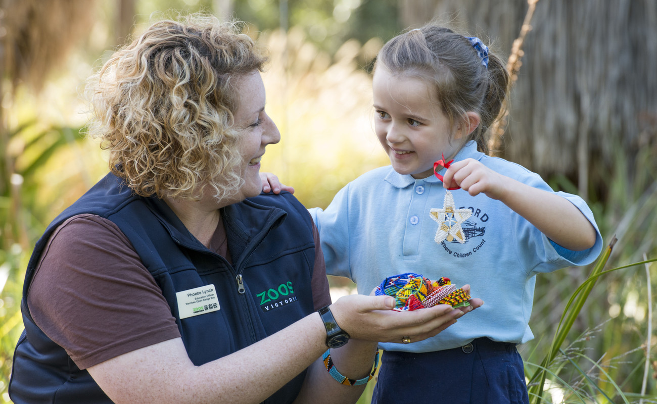 A Student with a ZV Educator, holding up her Beads for Wildlife craft creation.