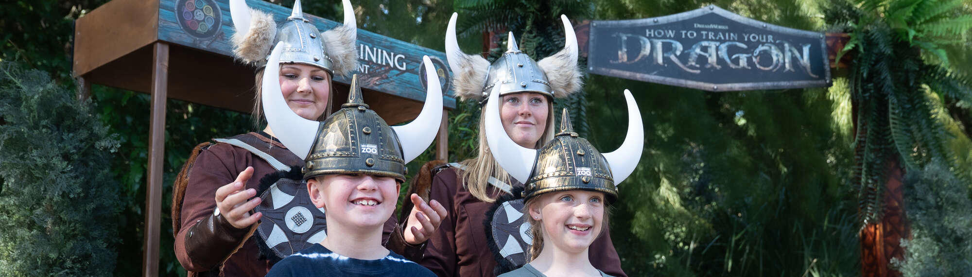 "How To Train Your Dragon"; Two young guests having their hair braided by two "Vikings," all smiling.