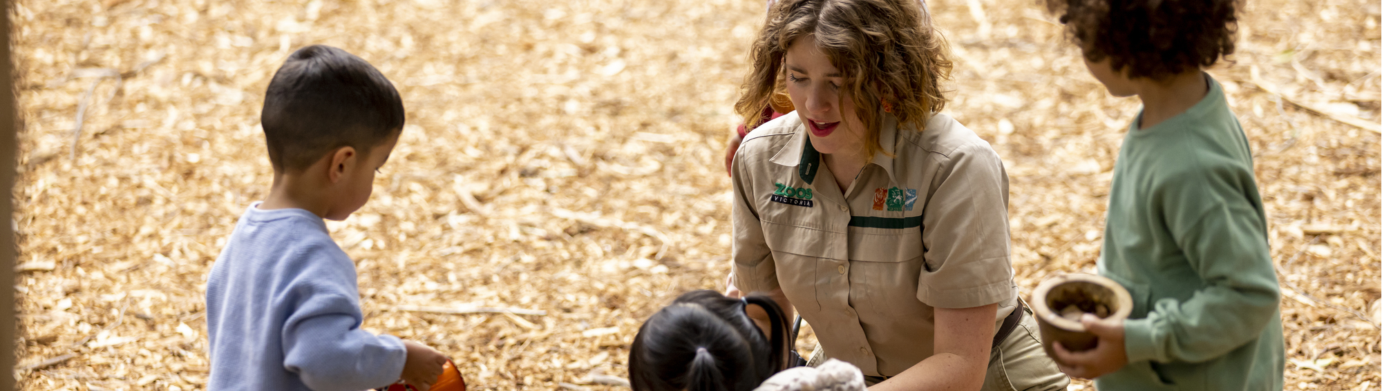 A Keeper interacts with four young guests in the bark-laden Adventure playground.