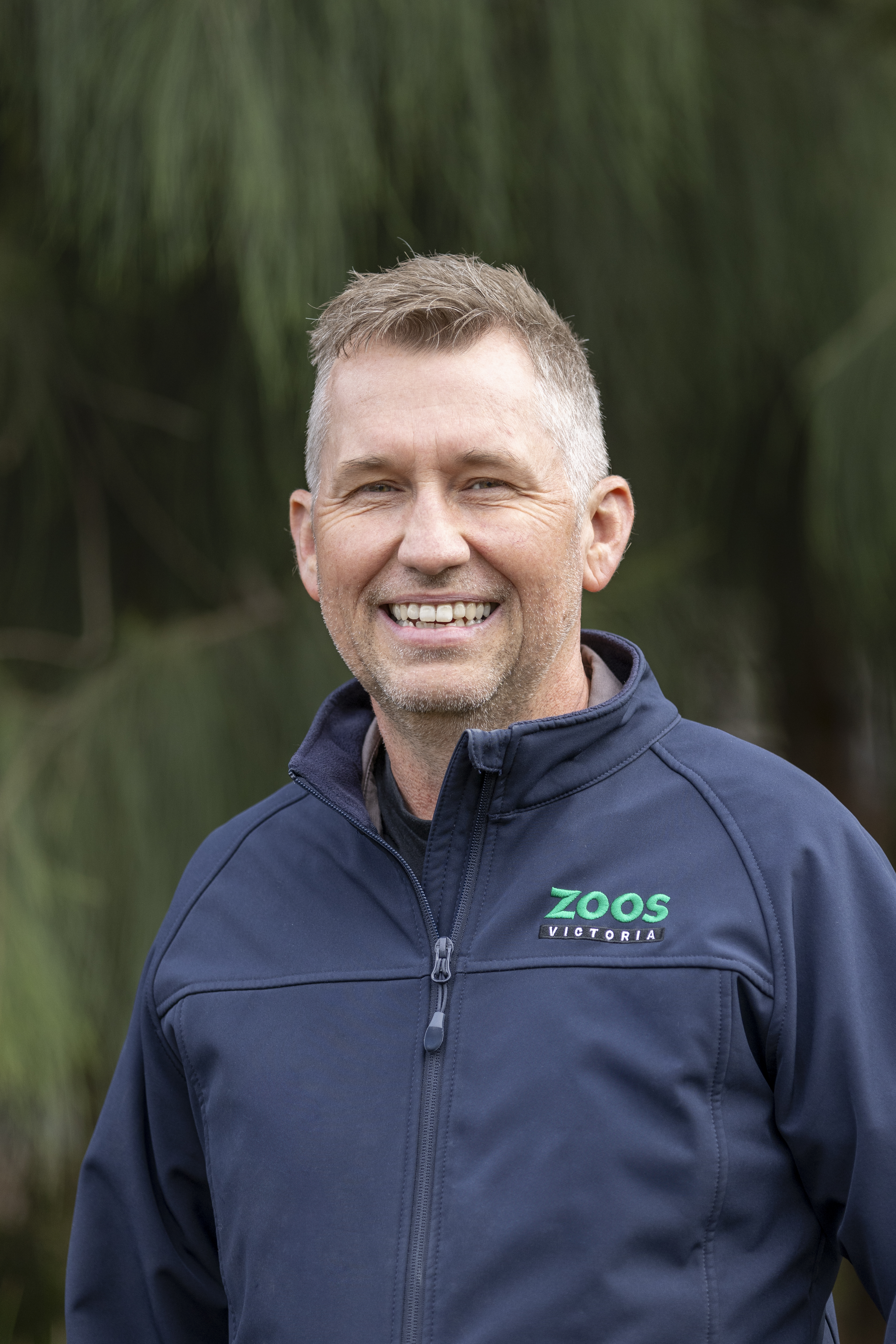 Portrait of Vet Garry, in front of a leafy backdrop.