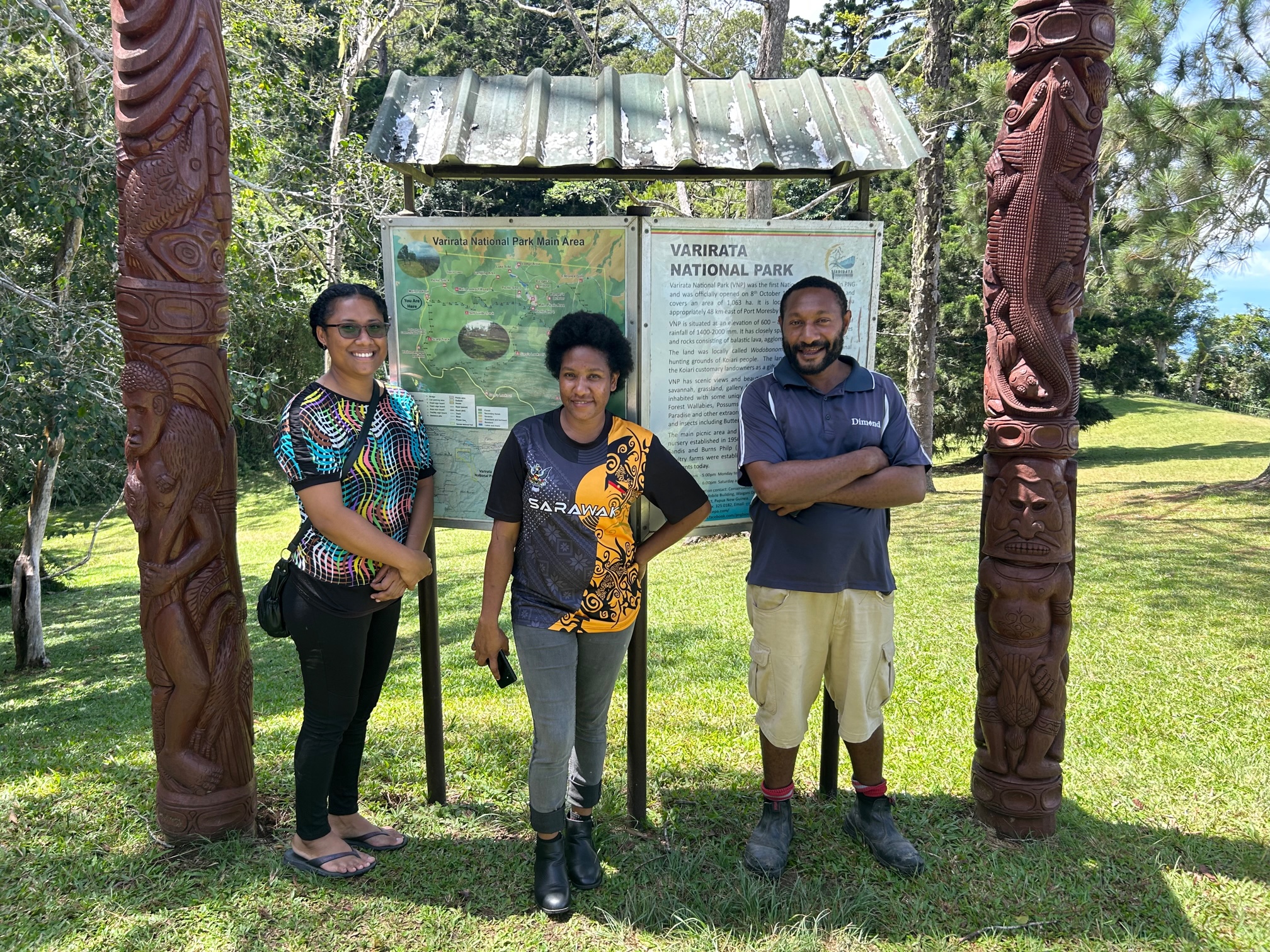 Three Papuans posing in front of a map-sign for Varirata National Park.