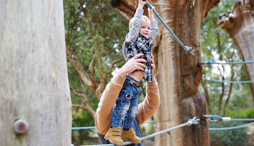 A young guest joyfully grabbing onto a thick, blue rope, while his parent is behind him, holding him up.